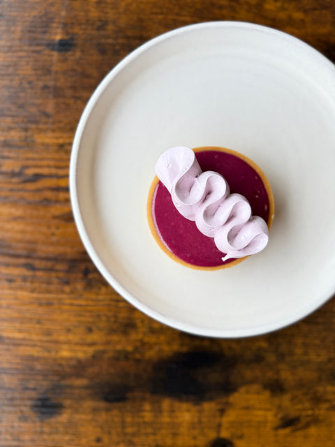 Blackcurrant tart topped with piped pink cream, served on a white plate at Krumb Bakery, Belfast