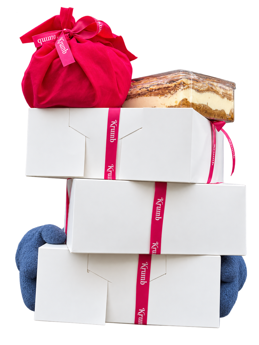 Three white Krumb Christmas boxes tied with pink ribbon, topped with Christmas pudding and tiramisu, held in blue gloved hands